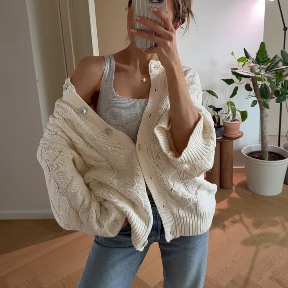 Person wearing a cream cardigan over a white tank top in a home setting.