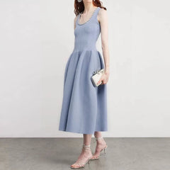 Woman wearing a light blue dress holding a clutch against a plain background