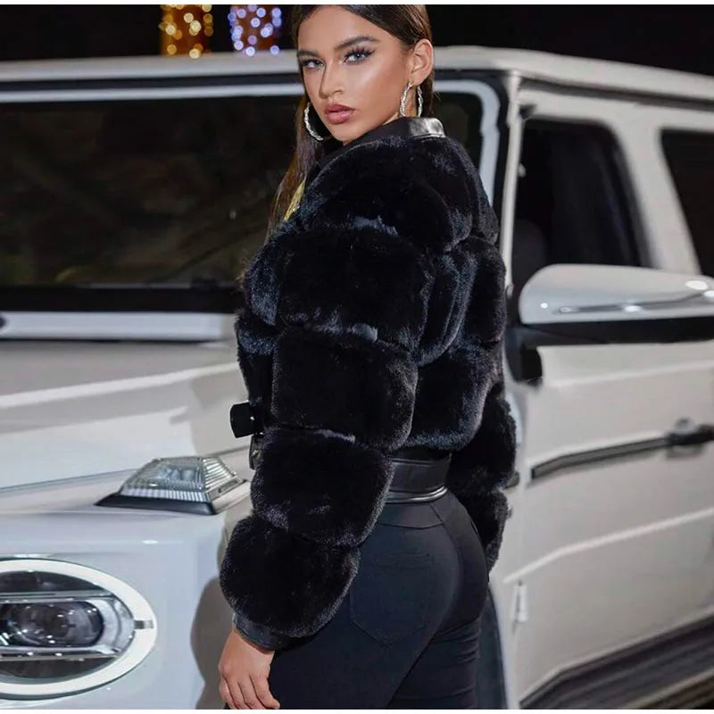 Woman in a black fur coat standing next to a white car at night.