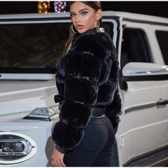 Woman in a black fur coat standing next to a white car at night.