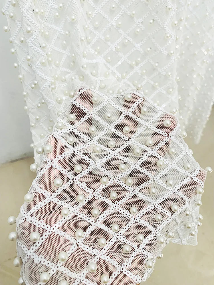 Close-up of a white lace fabric with pearl embellishments on a neutral background