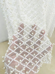 Close-up of a white lace fabric with pearl embellishments on a neutral background