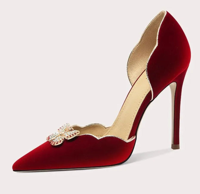 Red high-heeled shoe with decorative brooch on a light gray background