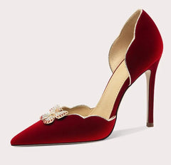Red high-heeled shoe with decorative brooch on a light gray background