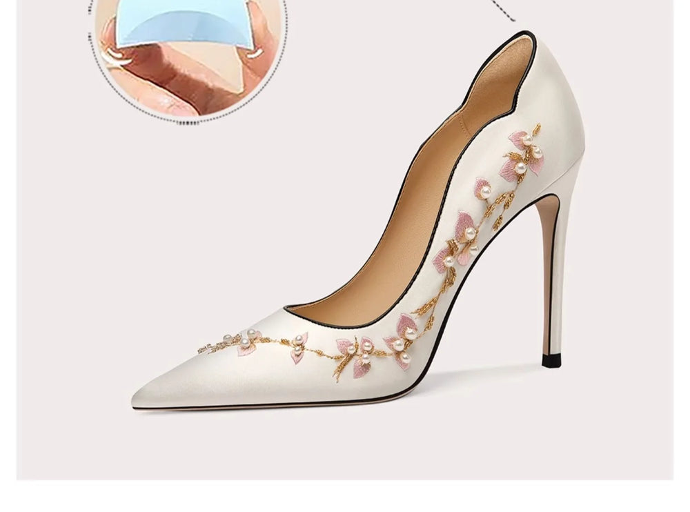 White high-heeled shoe with floral embroidery on a light gray background