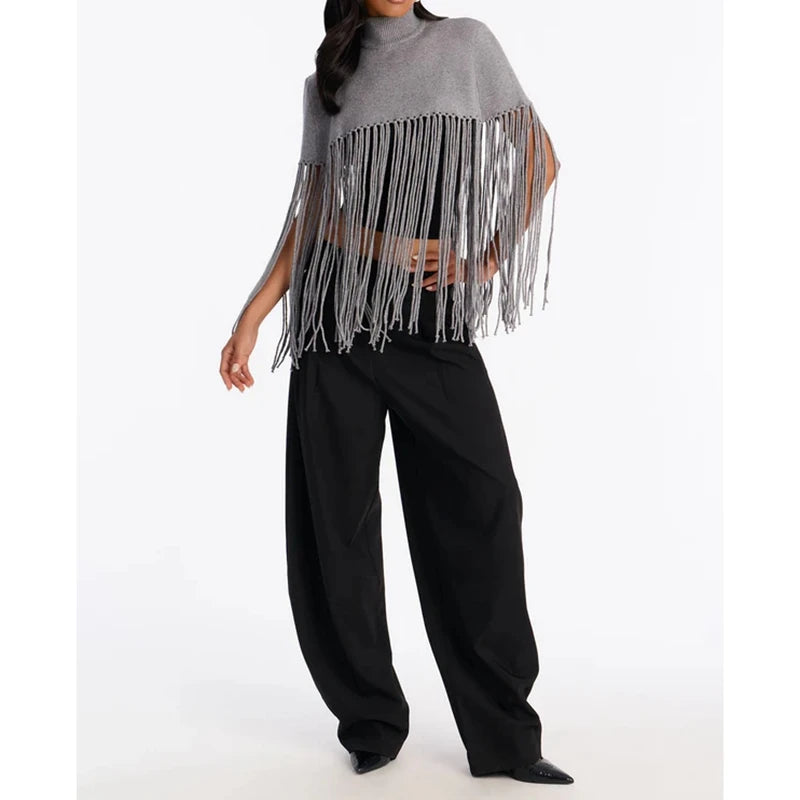 Model wearing a grey knit poncho with turtleneck and fringe