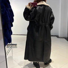 Person wearing a long black leather coat with white fur lining, taking a mirror selfie.