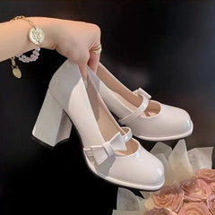 A pair of glossy white Mary Jane block-heel pumps held by a hand, with a bracelet and rings visible, set against a dark background with pink roses at the bottom right.