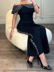 Woman in a black off-shoulder dress with white embellishments sitting on a white chair.