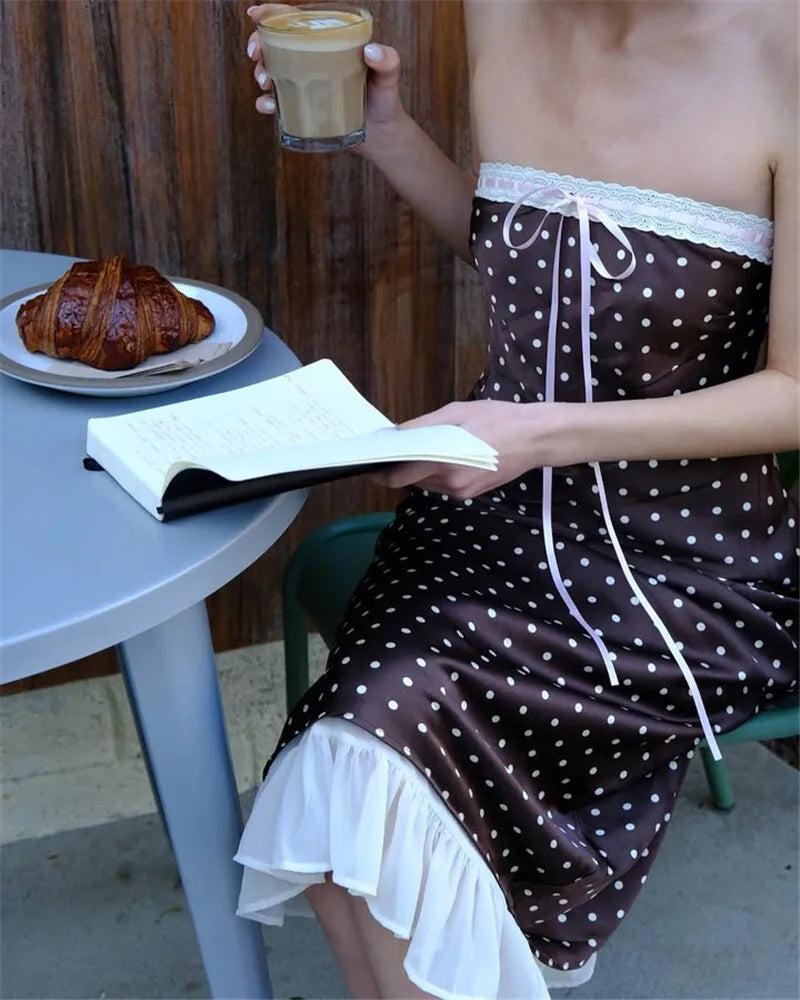 Person in a polka dot dress holding a glass of coffee and reading a book outdoors.
