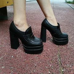 Feet wearing chunky platform block heel loafers on pavement