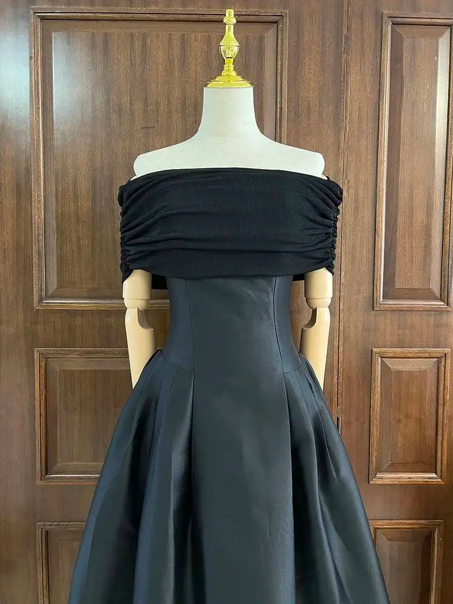 Black off-shoulder gown on a mannequin against a wooden panel background