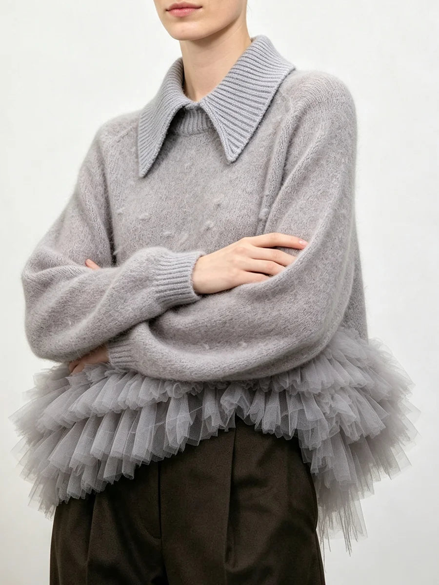 Gray knit sweater with a structured collar and a layered gray tulle ruffle detail at the waist, shown with crossed arms.