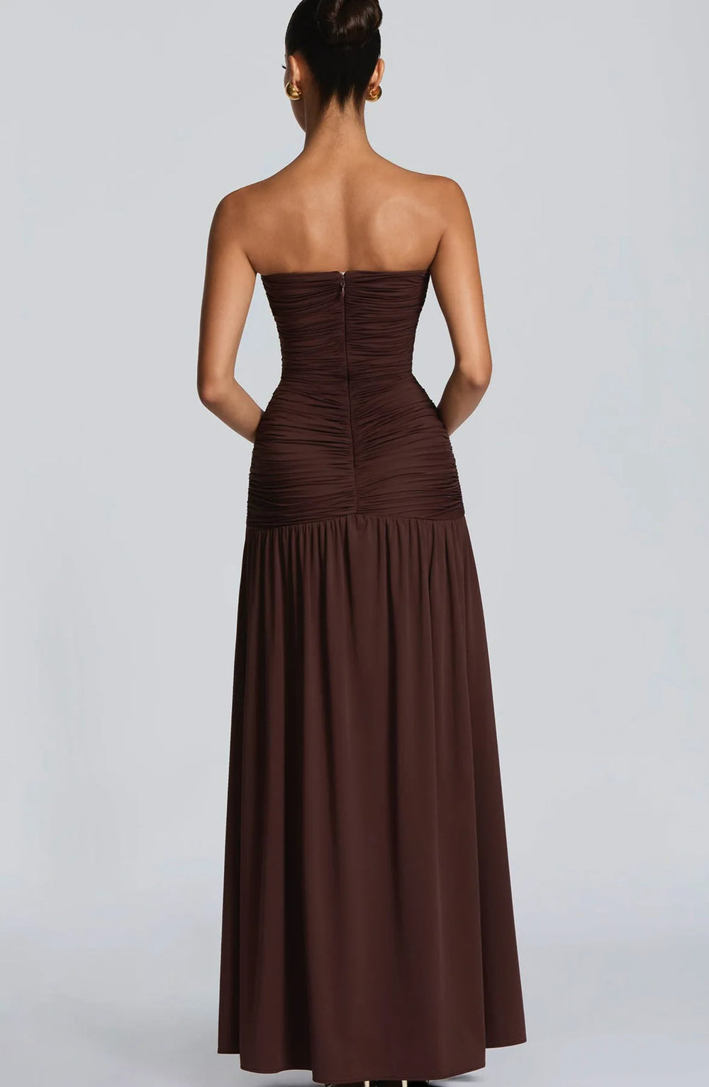Woman wearing a strapless brown dress on a plain background