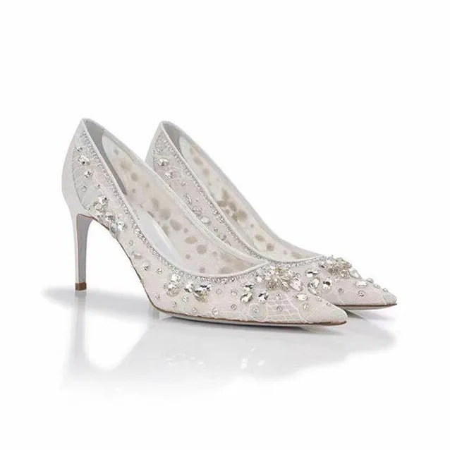 Pair of white high-heeled shoes with crystal embellishments on a white background