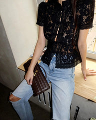 Person wearing a black lace top and light blue jeans, holding a brown handbag.