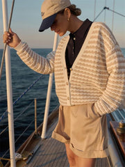 Person on a boat wearing a beige cardigan and cap, with water in the background