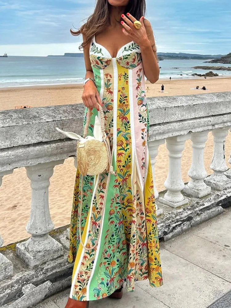 Woman in a colorful floral dress standing on a beach with ocean view.