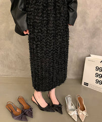 Person wearing a black textured dress with shoes on a gray floor.