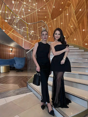Two women in black outfits standing on a staircase in an elegant interior setting.