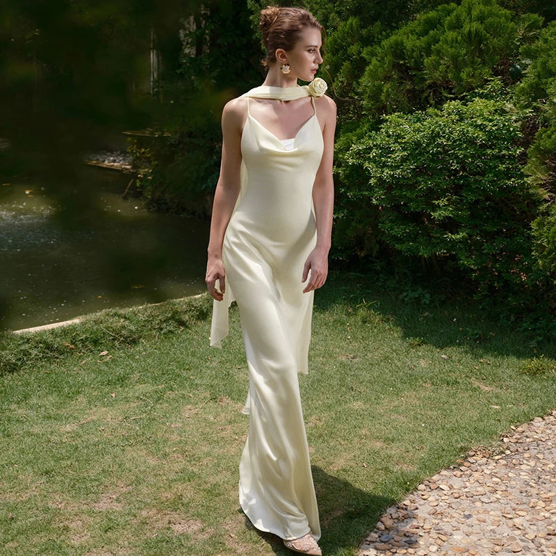 Woman in a white dress standing in a garden with greenery and a pond in the background