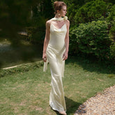 Woman in a white dress standing in a garden with greenery and a pond in the background