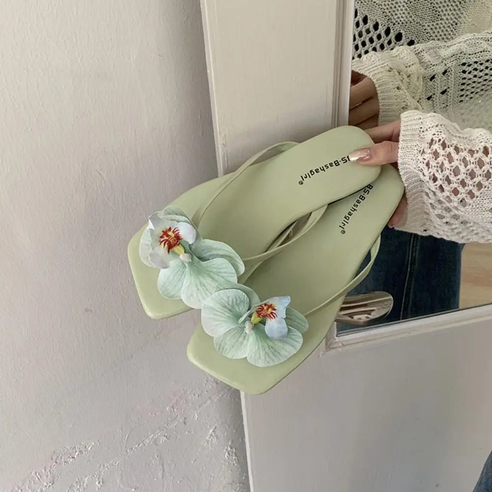 Light green sandal with floral design held by a person in front of a mirror.
