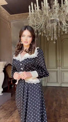 Woman in a polka dot dress standing in a room with a chandelier.