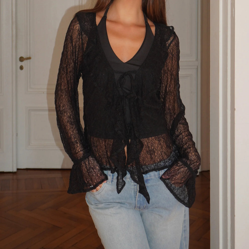 Person wearing a black lace top over a black shirt with light blue jeans indoors.