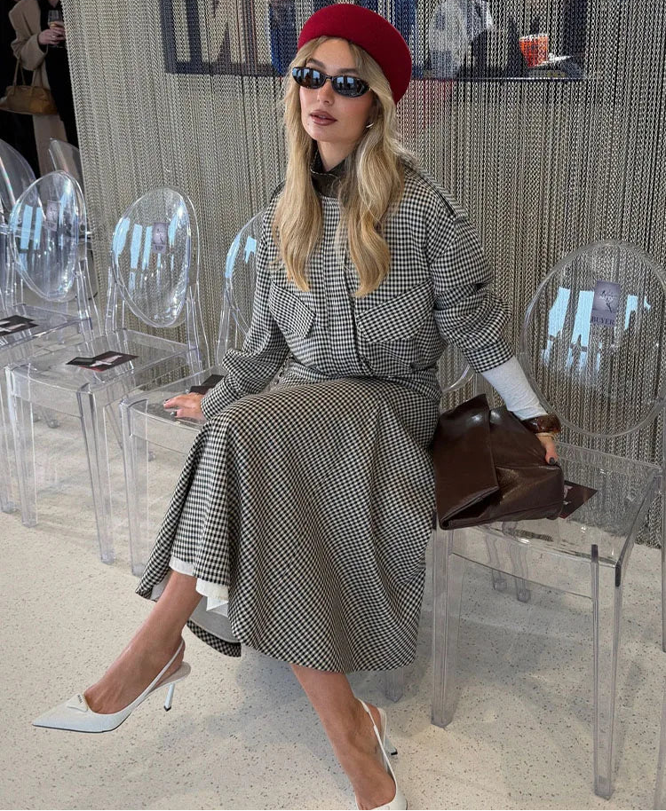 Woman in a checkered dress with a red beret and sunglasses sitting on a clear chair.