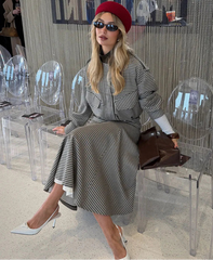 Woman in a checkered dress with a red beret and sunglasses sitting on a clear chair.