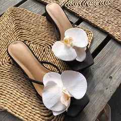 Black sandals with white orchids on a woven mat and wooden surface