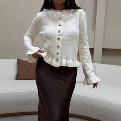 Woman wearing a white cardigan with decorative buttons in a living room setting.