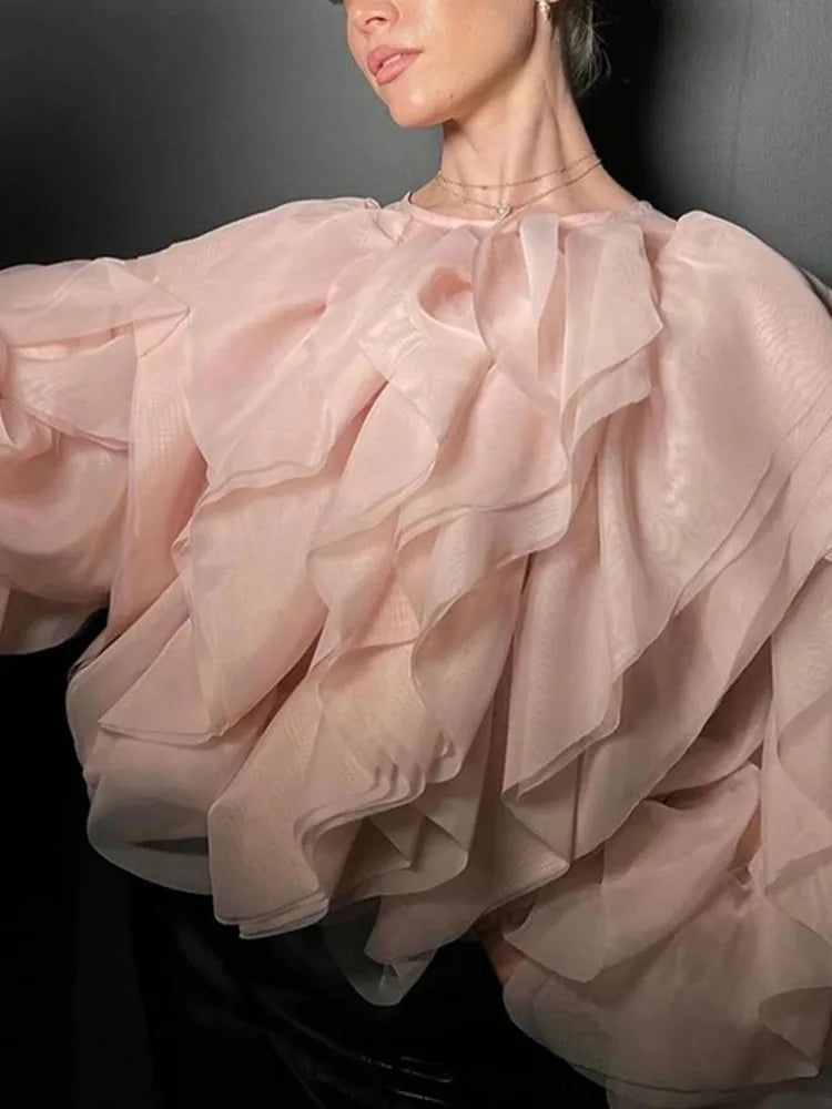 Close-up of a person wearing a light pink ruffled blouse against a dark background