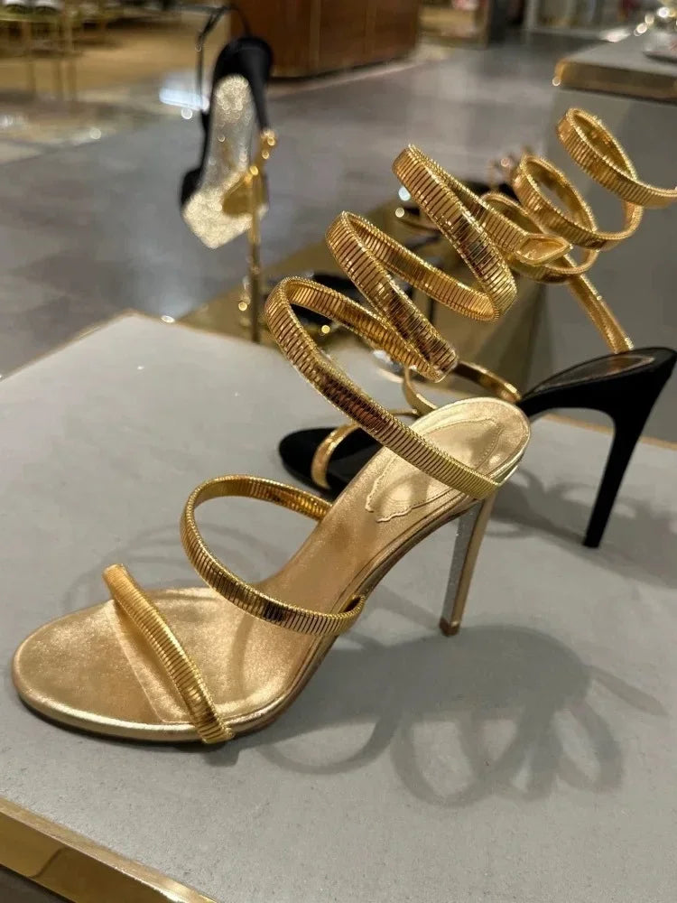 Gold high-heeled sandals on a reflective surface