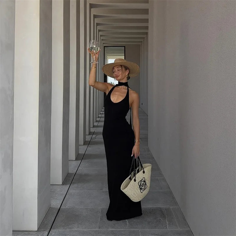 Woman in a black dress and straw hat holding a white bag in a geometric hallway.
