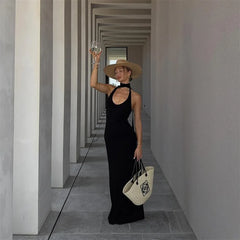 Woman in a black dress and straw hat holding a white bag in a geometric hallway.