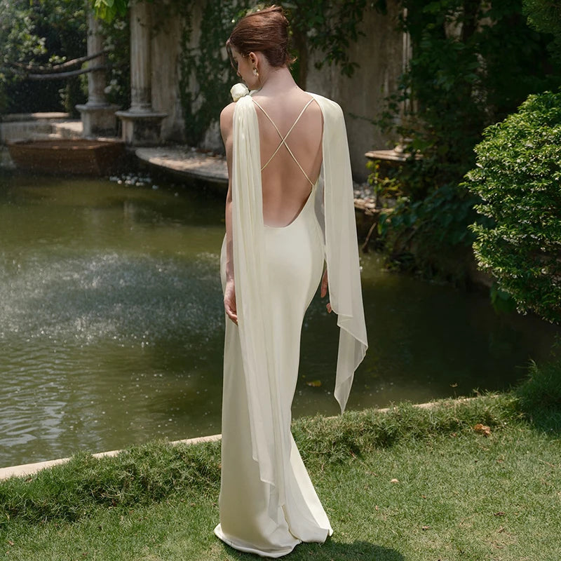 Woman in a white gown standing by a pond with greenery around