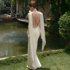 Woman in a white gown standing by a pond with greenery around