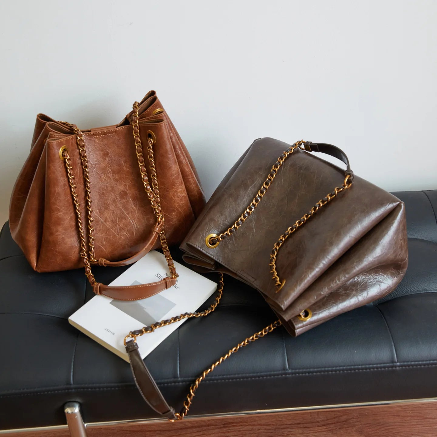 Two brown leather handbags with gold chains on a black surface.