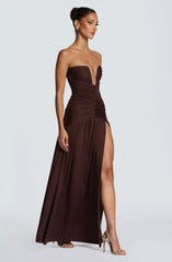 Woman wearing a strapless brown evening gown with a slit on a white background