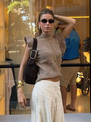 Woman wearing a brown knit top and white pants standing in front of a store window.