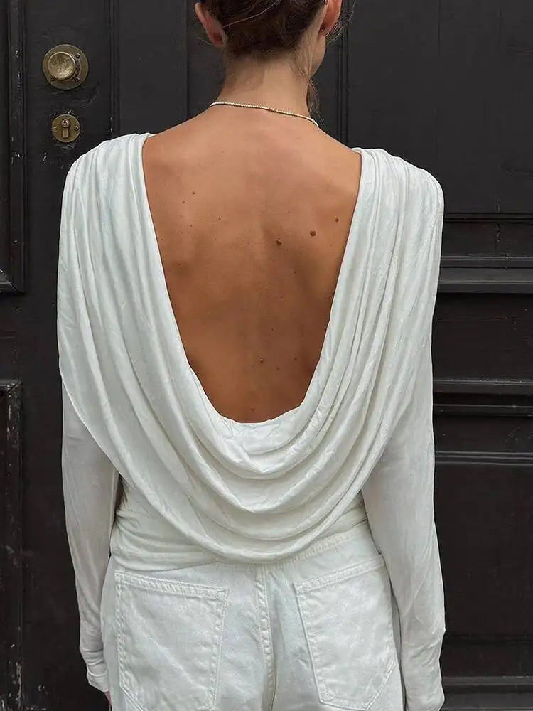 Person wearing a white open-back top and pants in front of a dark door.