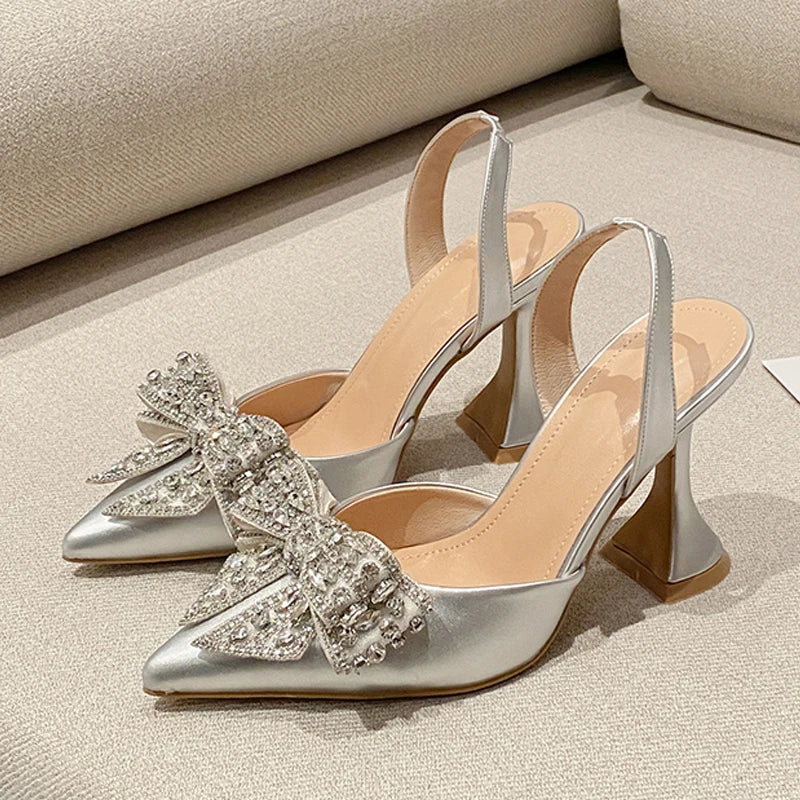 Silver high-heeled shoes with decorative bow on a light background