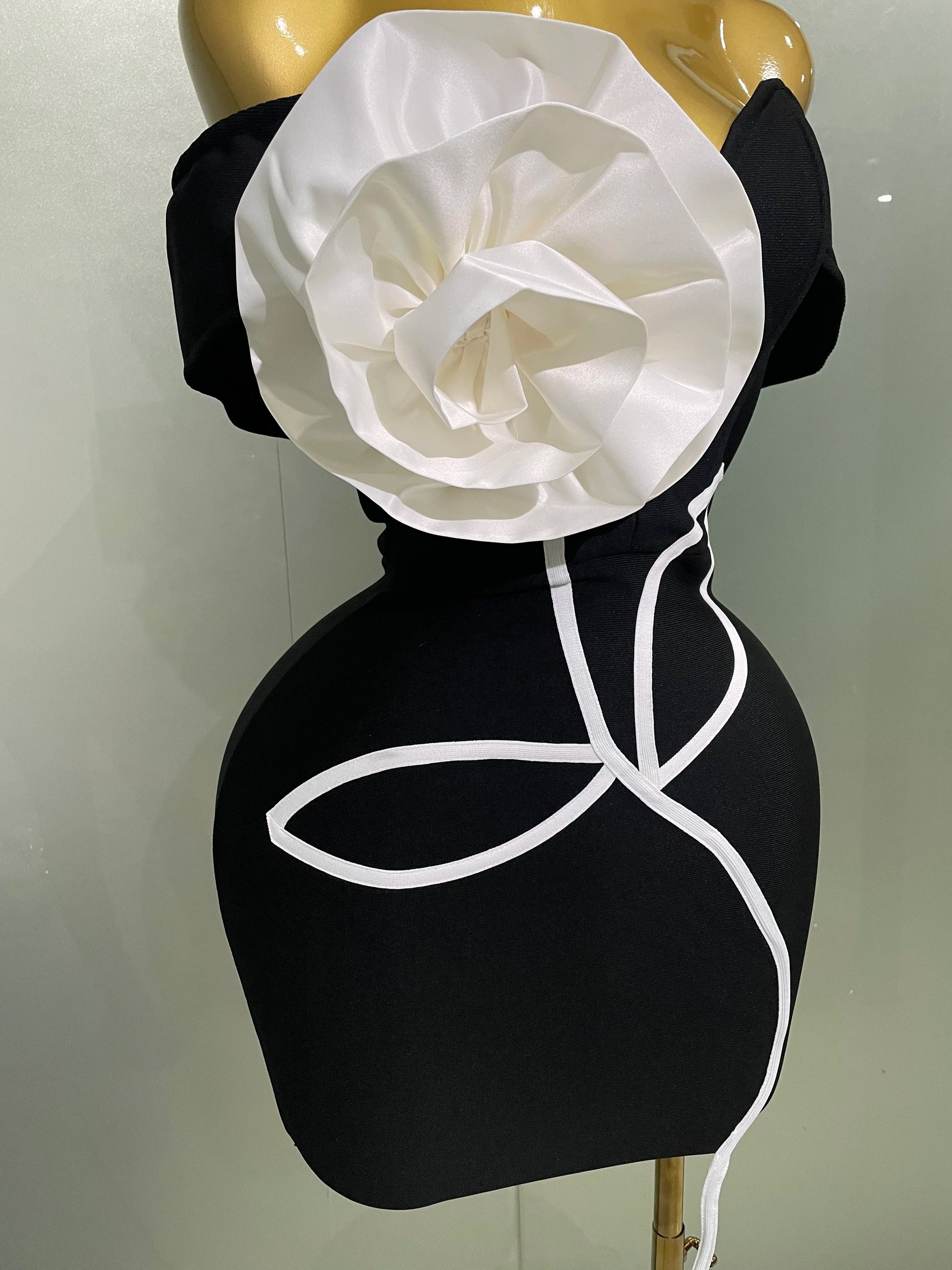 Black dress with a large white flower on a mannequin against a plain background