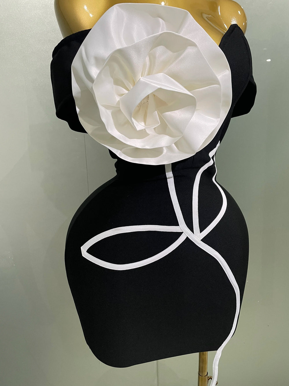 Black dress with a large white flower on a mannequin against a plain background