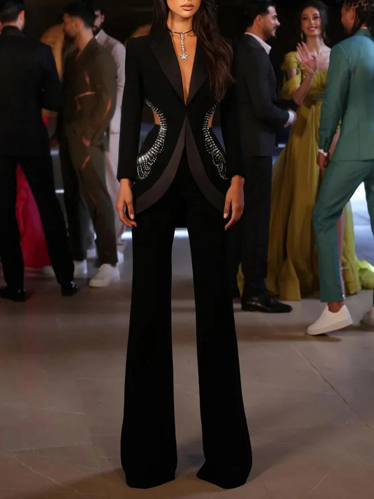 Person wearing a black suit with a unique design on a blurred background of people socializing.