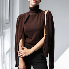 Woman wearing a brown turtleneck sweater and cape with button details on a light background