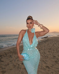 Woman in a light blue dress standing on a beach at sunset