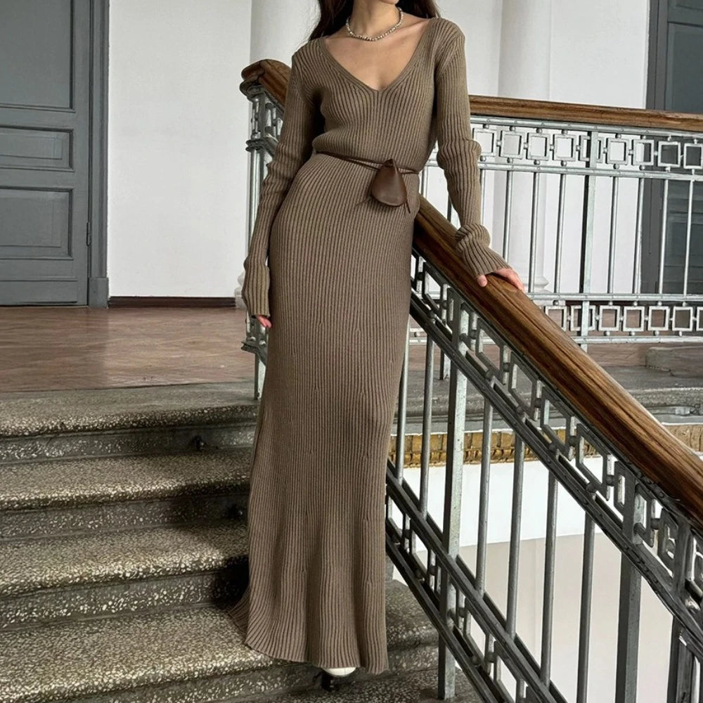 Woman in a long brown ribbed dress standing on a staircase.